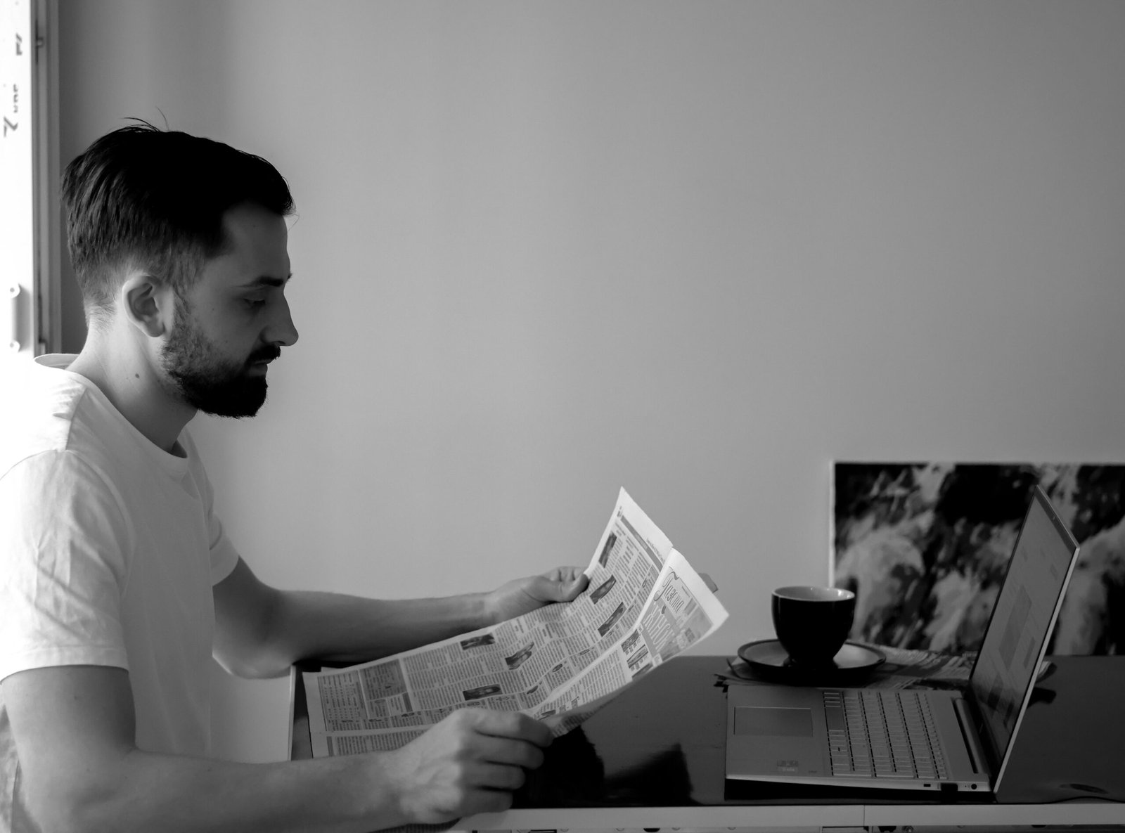 Man sitting at a desk with an open laptop and coffee, reading