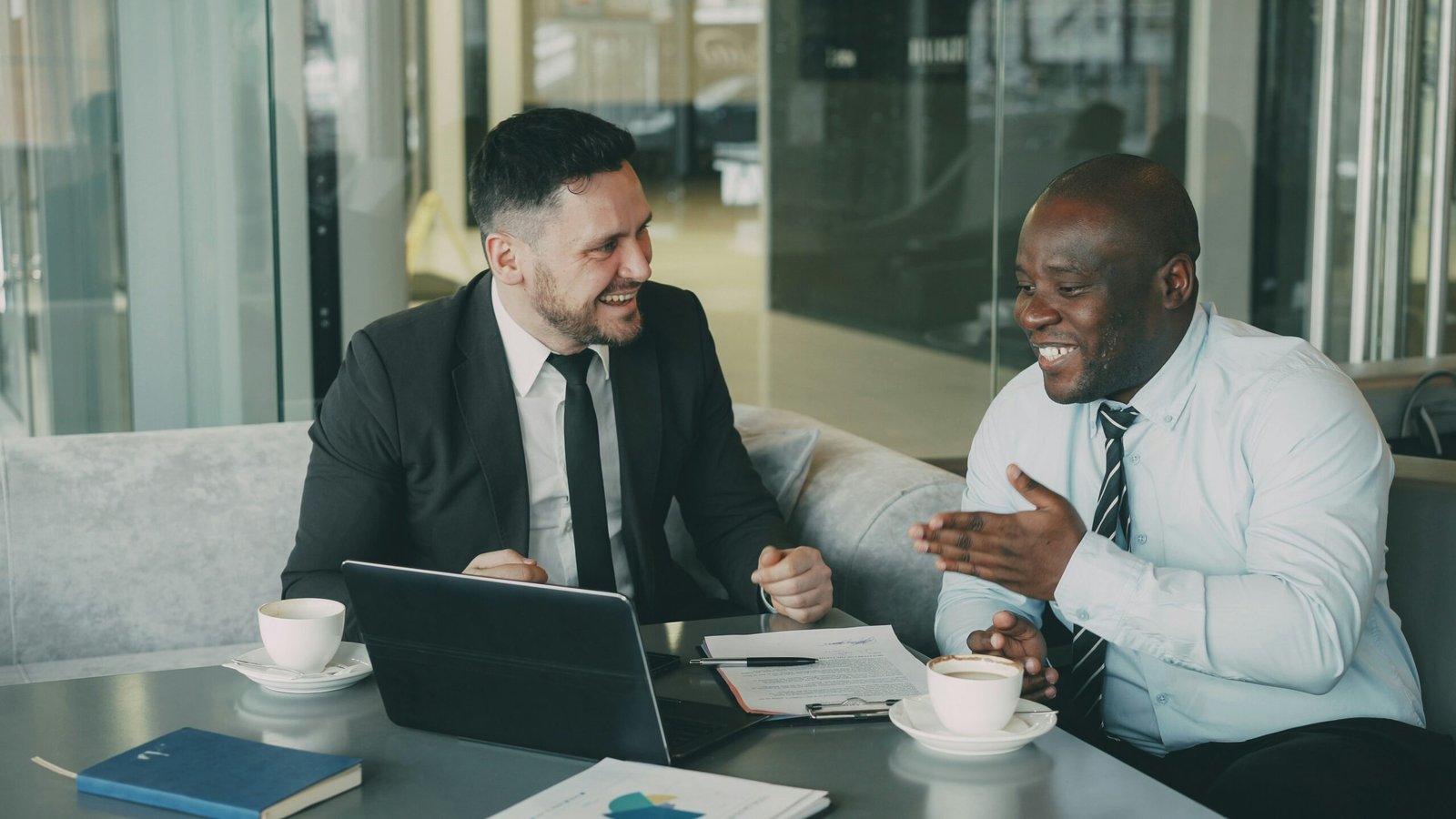Two businessmen smiling and chatting over coffee with a laptop on the table