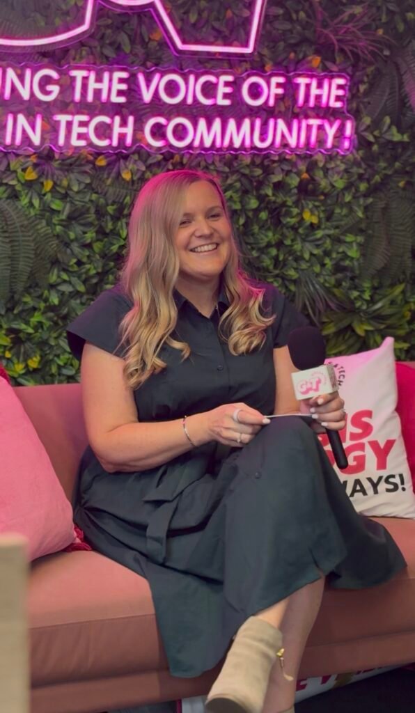 Holly Rae sitting on a sofa with a microphone, talking and smiling, during an interview at the Girls and Tech of Tomorrow Career Lab